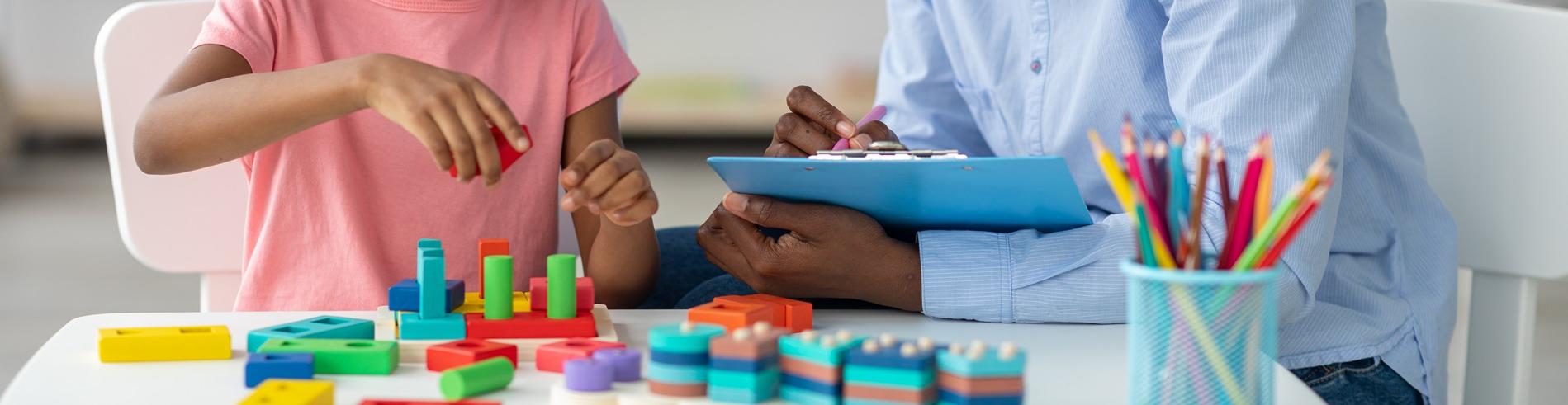 An ABA practitioner works with a child who is stacking blocks