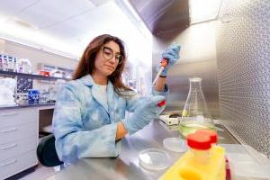 A woman student in a lab coat and protective eyewear works in the lab.