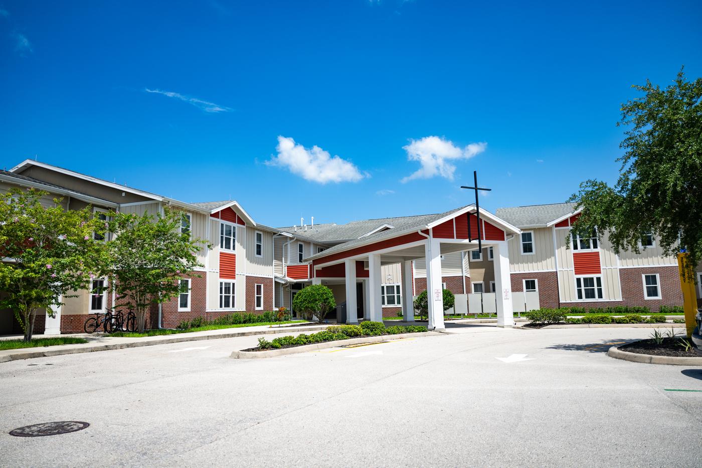 Entrance to Mary Star of the Sea Newman Hall on a bright sunny day. A covered entryway sits in the centre of the building with a cross on top.